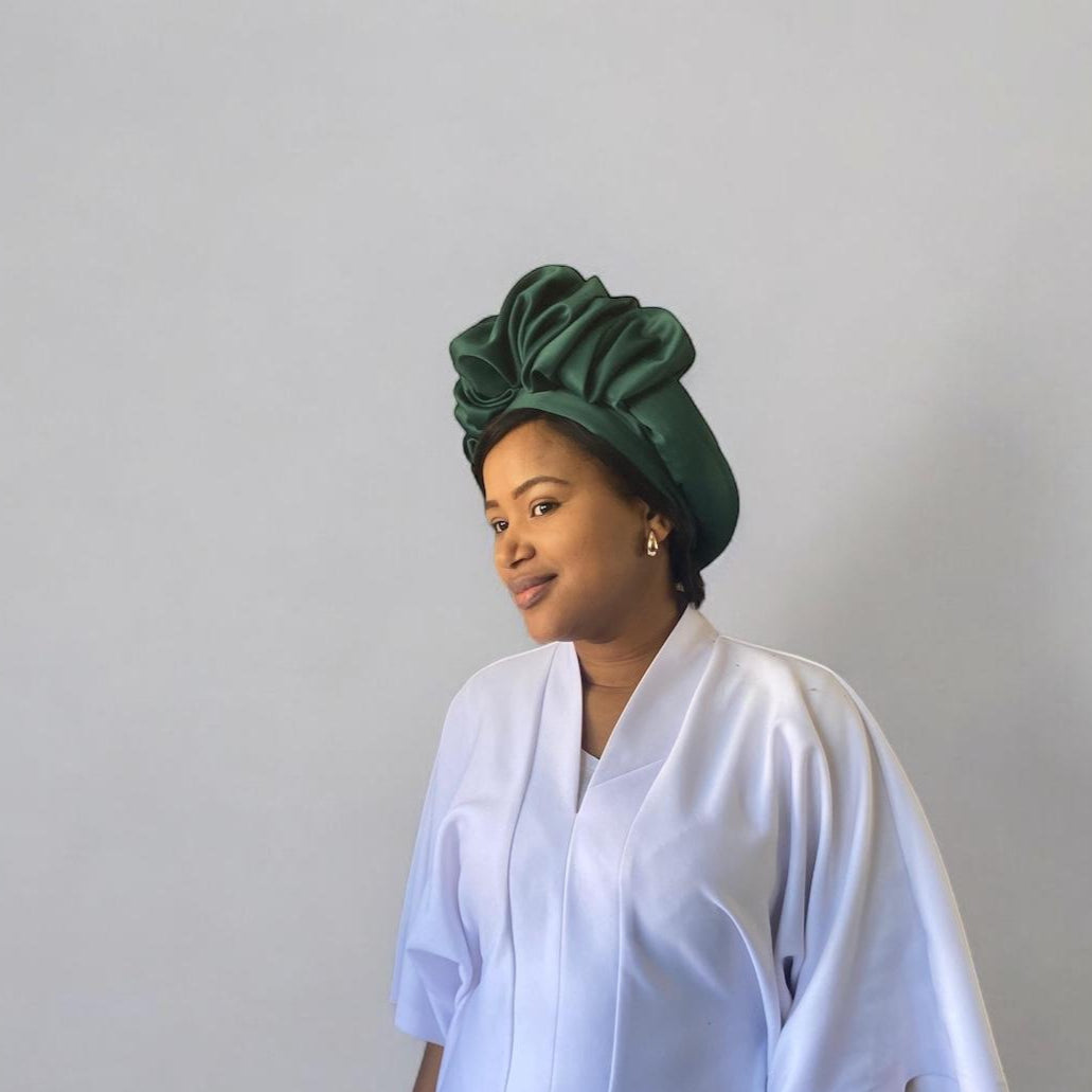 Woman wearing a green headwrap and white outfit against a plain background