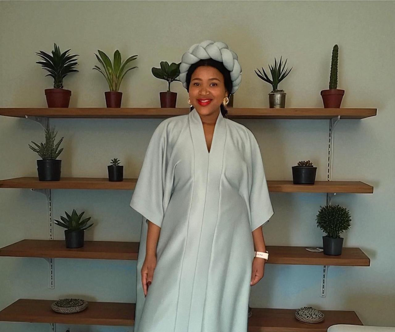 Woman in a light blue dress standing in front of wooden shelves with plants.